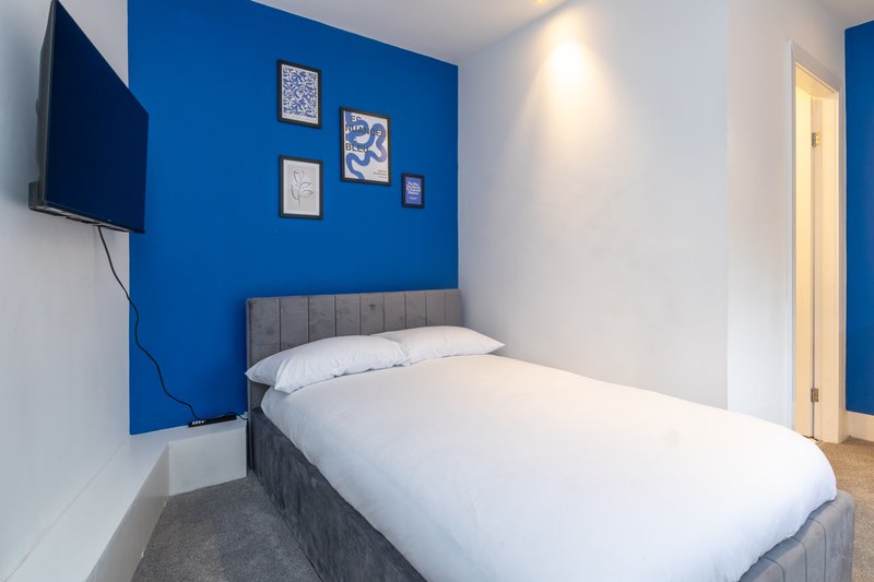 Modern bedroom with single bed, blue accent wall, mounted TV, and framed wall art