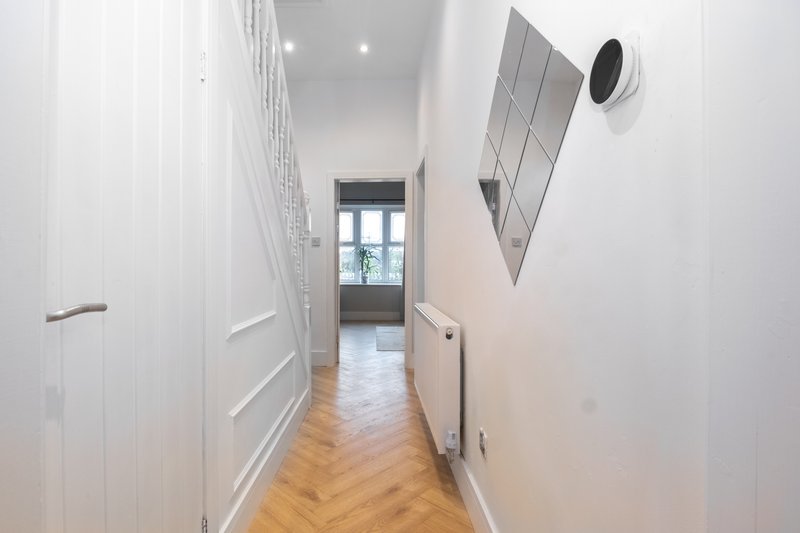 Narrow hallway with white walls, wooden floor, and modern heating controls