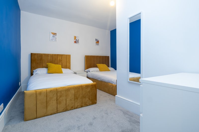Twin bedroom with wooden bed frames, yellow cushions, white bedding, and blue accent walls