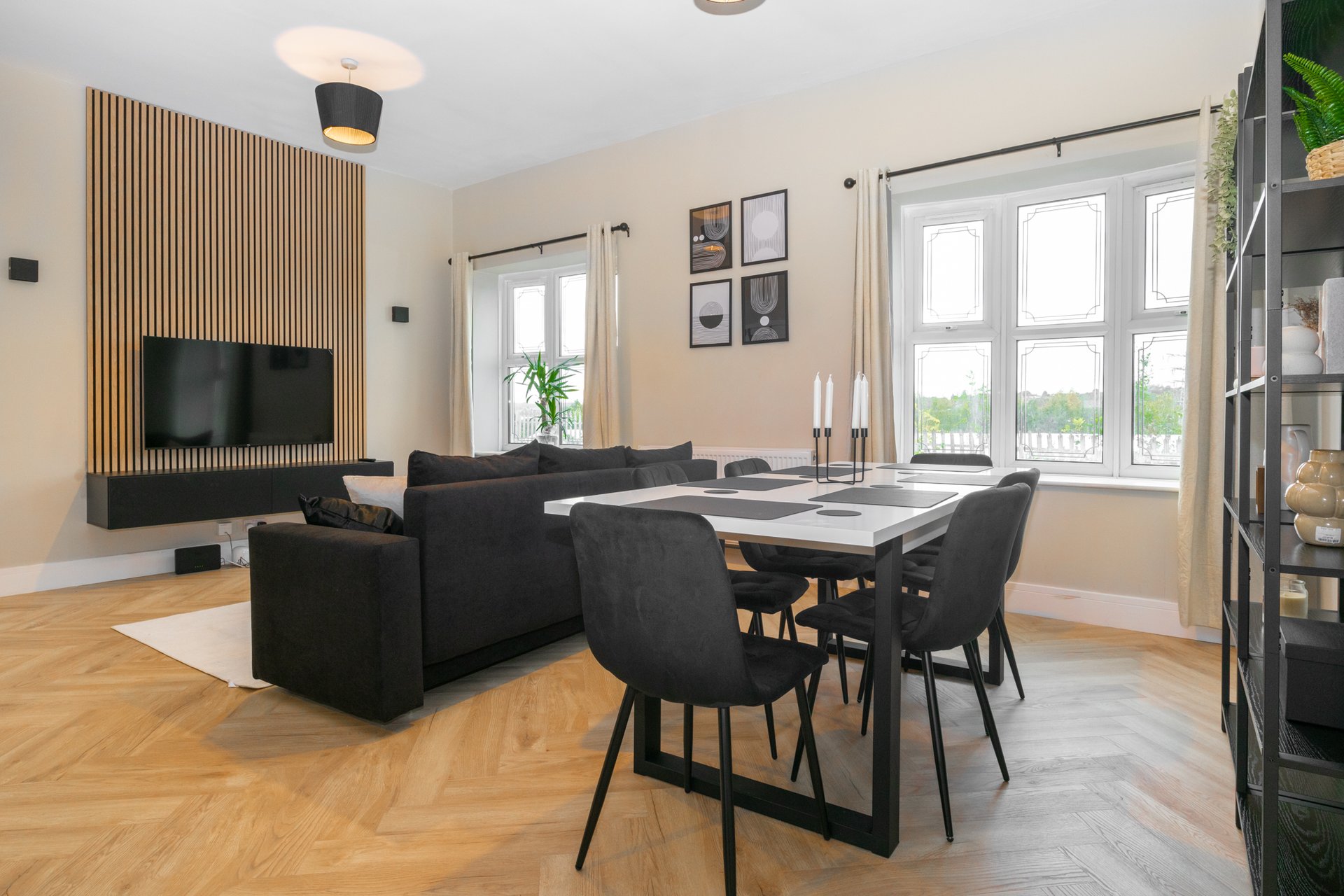 Modern open-plan living room with black sofa, dining table, wooden floor and large windows
