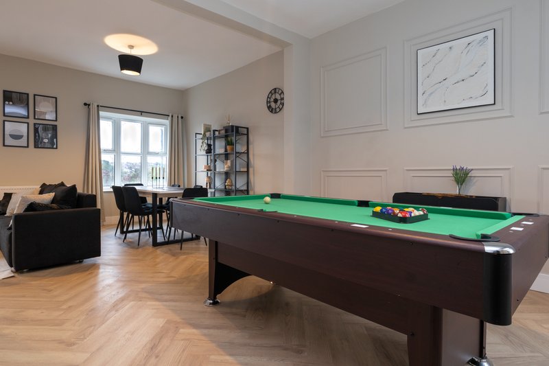 Open-plan living room with pool table, sofa, dining area and large windows