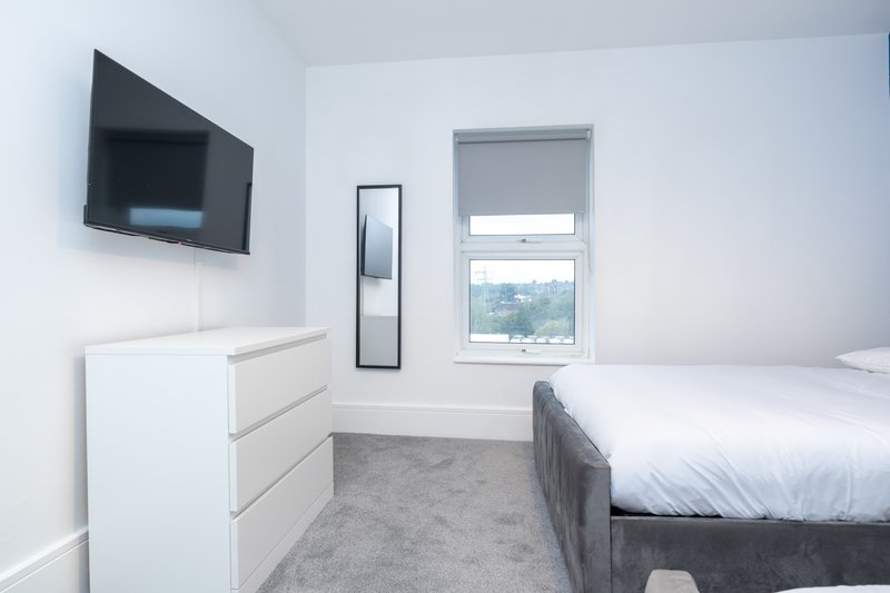 Modern bedroom with double bed, white dresser, wall-mounted TV and window overlooking landscape