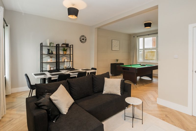 Open-plan living room with black sofa, dining area, pool table, and wooden flooring