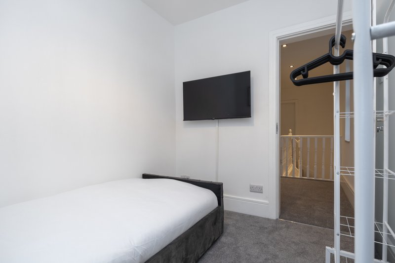 Compact bedroom with single bed, wall-mounted TV, and ensuite bathroom visible