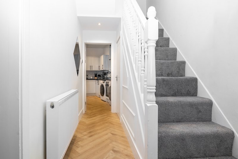 Hallway with wooden floor, white walls, staircase with gray carpet runner