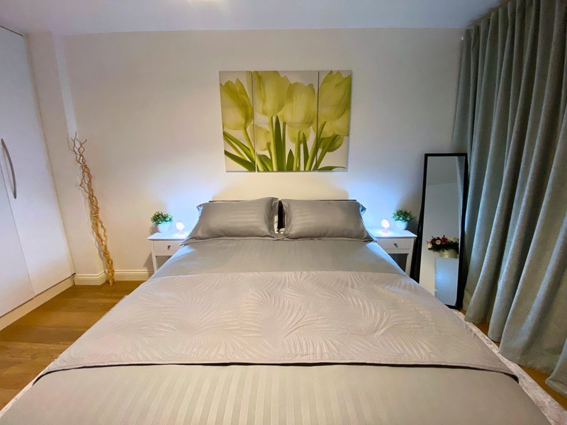 Modern bedroom with double bed, grey bedding, yellow flower artwork, and green curtains