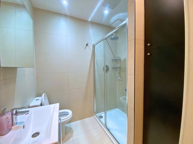 Modern bathroom with white tiles, glass shower enclosure, sink and toilet