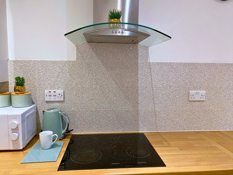 Modern kitchen with induction hob, glass cooker hood, wooden countertop and tiled splashback