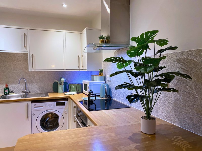 Modern kitchen with white cabinets, wooden countertop, washing machine, and potted plant