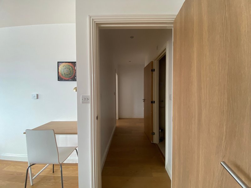 Hallway with wooden flooring, white walls, open doorway, and small framed artwork