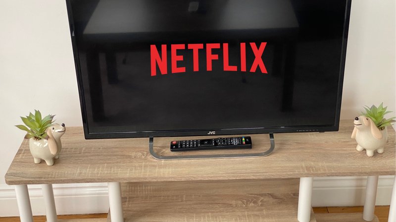 TV on wooden stand with remote, potted plants, and white legs visible