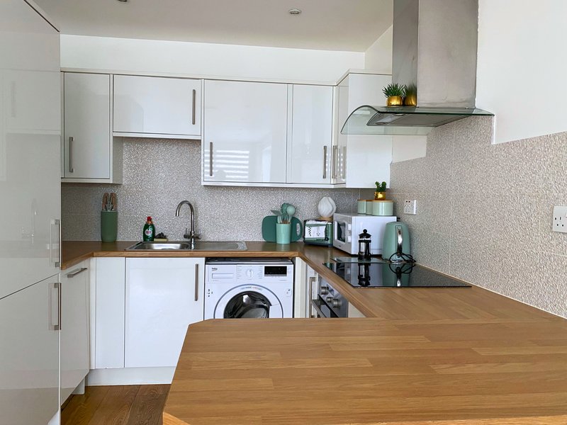 Modern kitchen with white cabinets, wooden countertop, integrated washing machine and stainless steel appliances