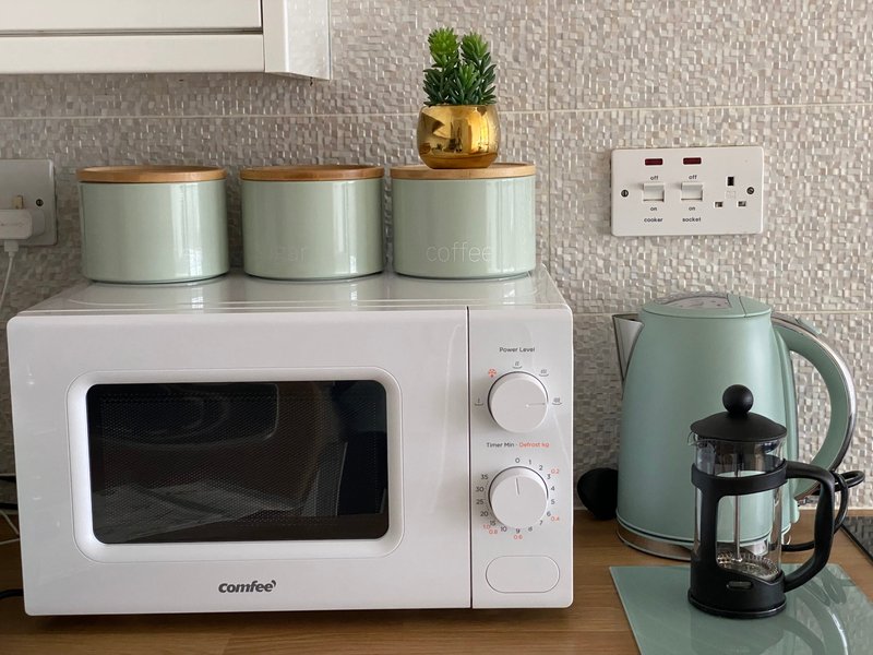 Kitchen counter with white microwave, kettle, storage containers and potted plant