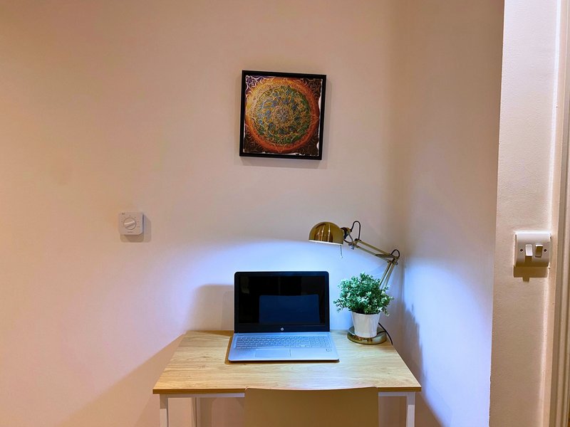 Compact home office desk with laptop, desk lamp, small plant and framed wall art