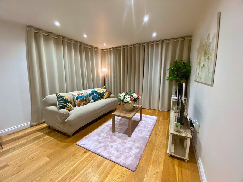Modern living room with cream sofa, wooden floor, lavender rug and floor-to-ceiling curtains