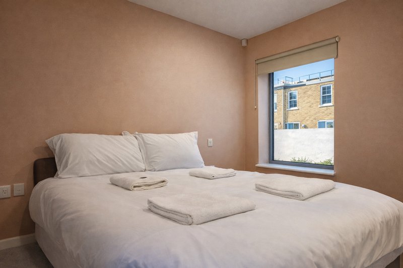 Bedroom with double bed, white bedding, pillows, and window overlooking brick building