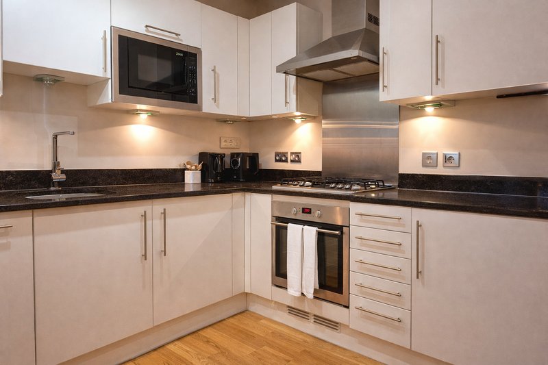 Modern kitchen with white cabinets, black countertop, stainless steel appliances and wooden flooring