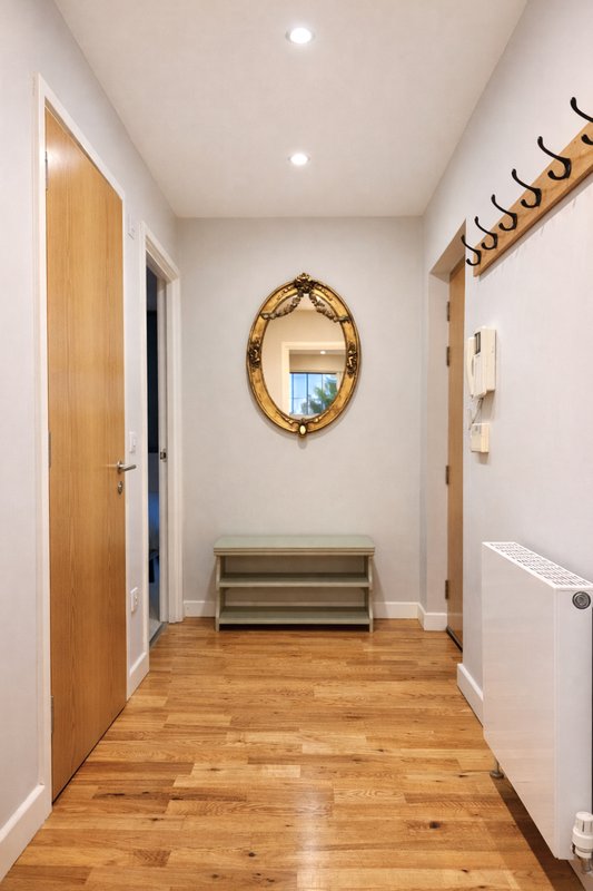 Bright hallway with wooden floor, gold-framed mirror, coat hooks and white walls