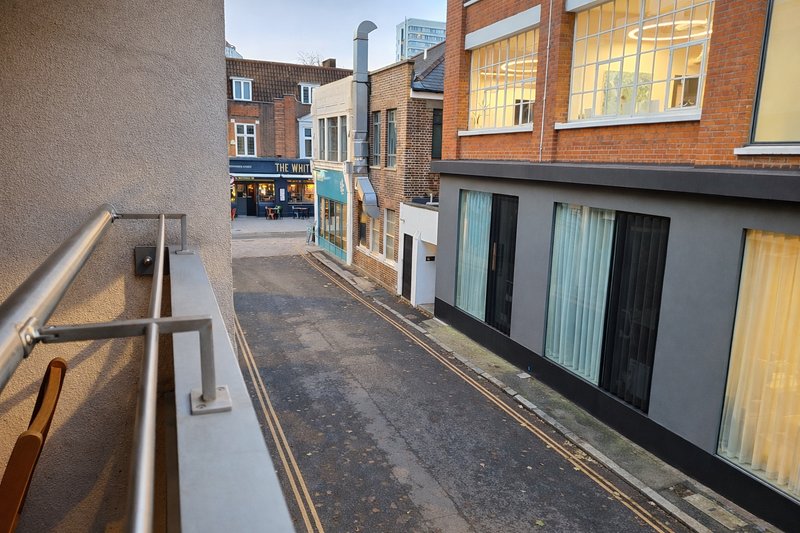 Narrow alley between brick buildings with metal railings and modern storefronts