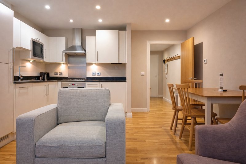 Open-plan kitchen and living area with white cabinetry, grey armchair and wooden dining table