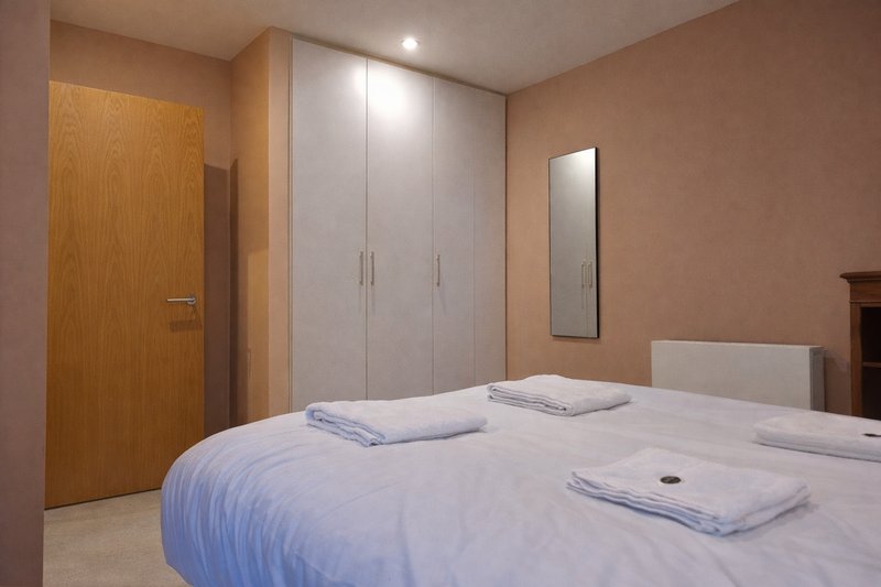 Modern bedroom with double bed, white wardrobe, wooden door and wall mirror