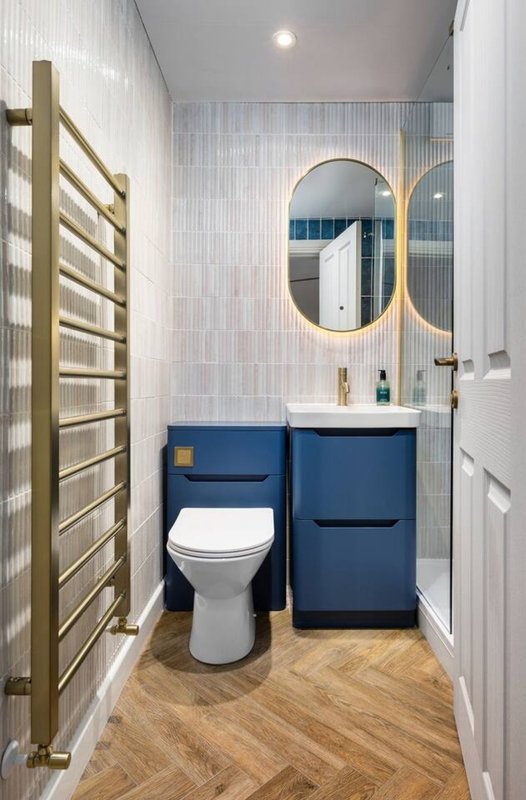 Modern bathroom with blue vanity, white toilet, gold-framed mirror and heated towel rail
