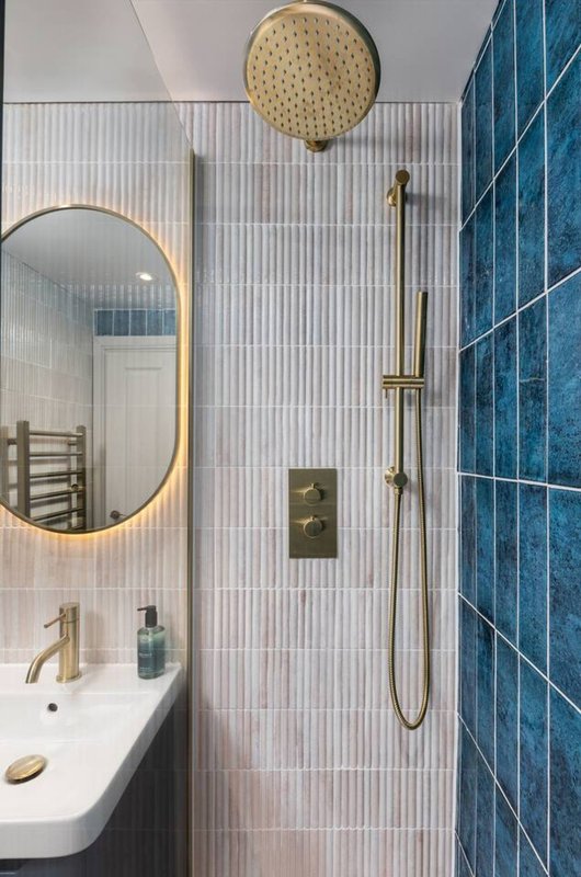 Modern bathroom with walk-in shower, round mirror, white sink and brass fixtures