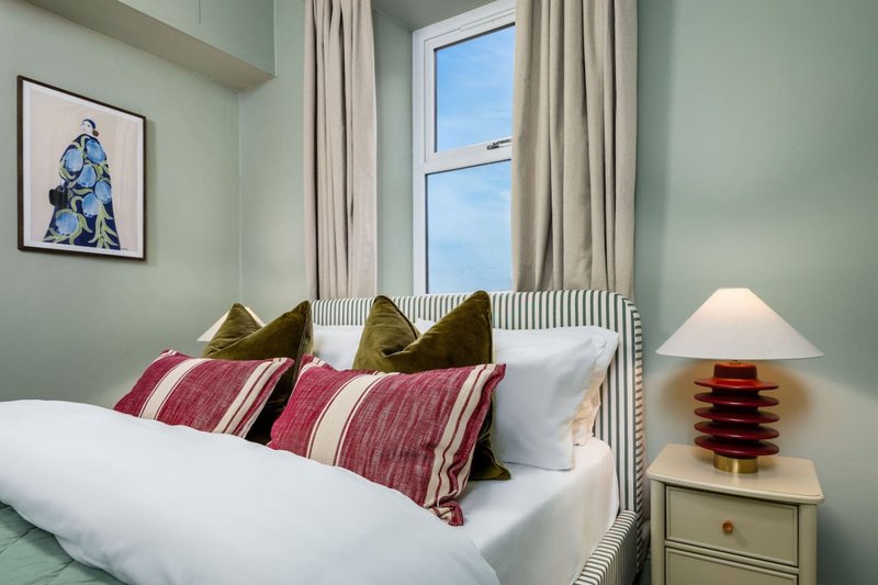 Bedroom with double bed, striped cushions, wooden lamp, window with curtains and framed artwork