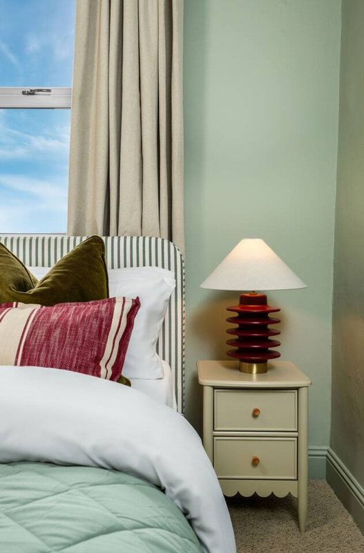 Bedroom with double bed, green headboard, bedside lamp and cream curtains