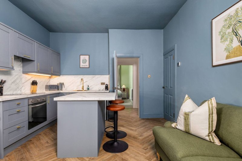 Open-plan kitchen and living area with blue walls, marble countertop, and green sofa