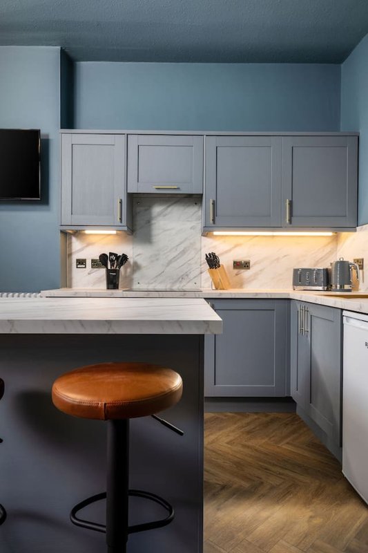 Modern kitchen with gray cabinetry, marble backsplash, island with wooden stool, and under-cabinet lighting