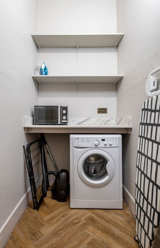 Compact laundry room with washing machine, microwave, shelving and wooden flooring