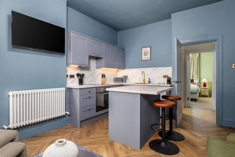 Modern kitchen with blue cabinetry, marble countertop, island seating, and open-plan living area