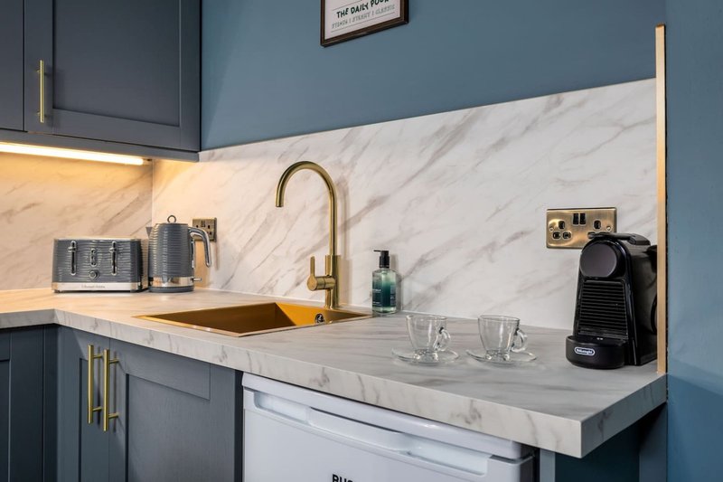 Modern kitchen with marble countertop, brass tap, gold-framed mirror and blue cabinetry