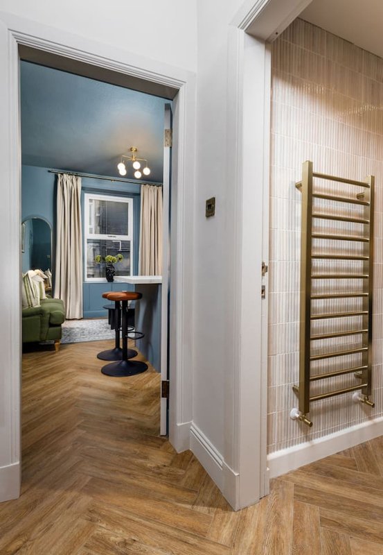 Modern hallway with wooden flooring, white walls, open doorway to blue bedroom, and heated towel rail