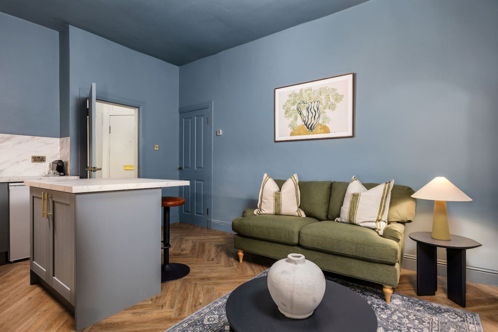 Open-plan living room with olive green sofa, kitchen island, and blue-painted walls