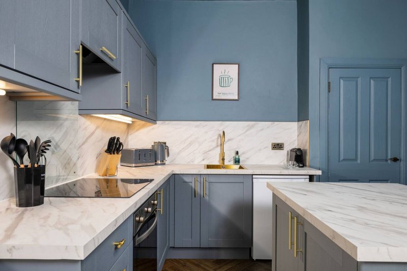 Modern kitchen with blue cabinetry, marble countertops, gold hardware and stainless steel appliances