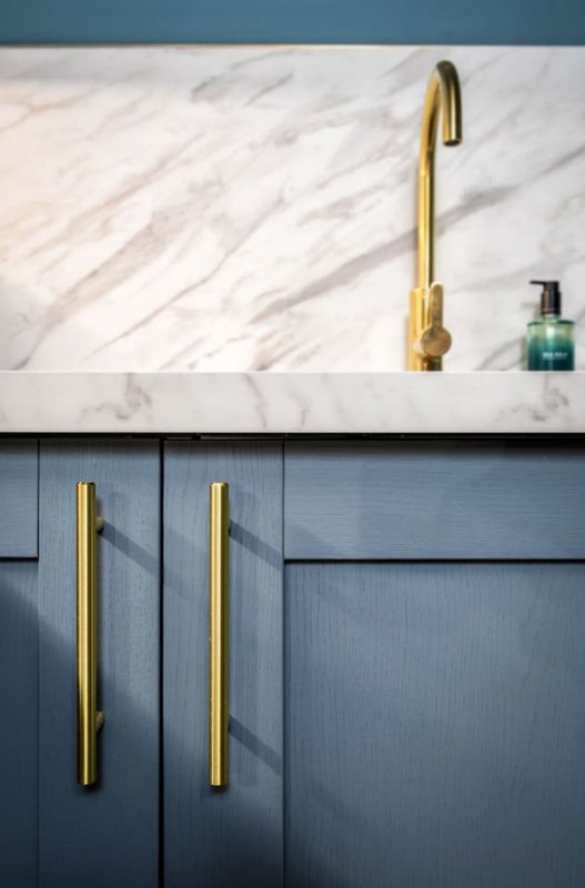 Modern kitchen with marble backsplash, gold tap, blue cabinetry and soap dispenser