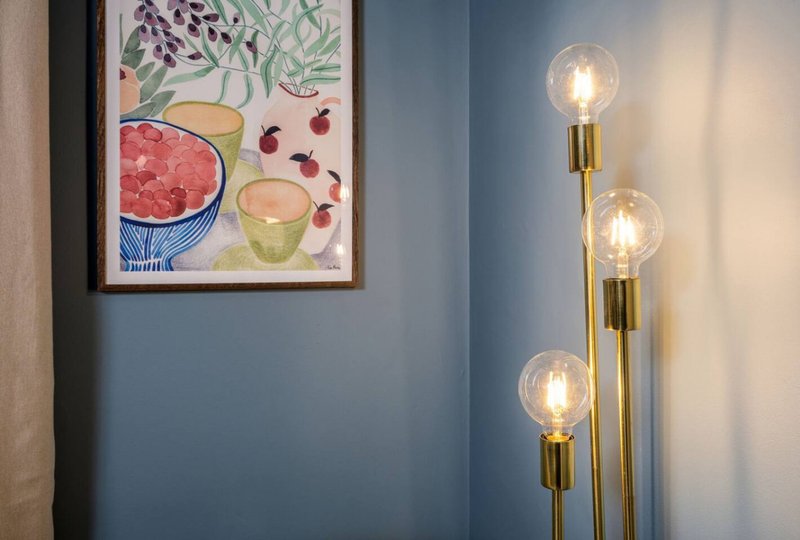 Blue-grey wall with framed fruit and botanicals artwork and brass floor lamp with three illuminated globe bulbs