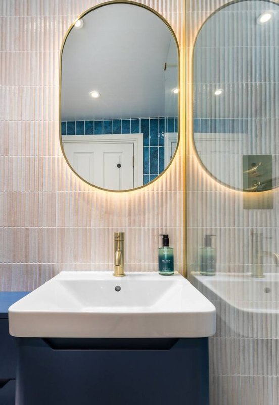 Modern bathroom with white sink, dark vanity, oval mirrors, and blue tile accents