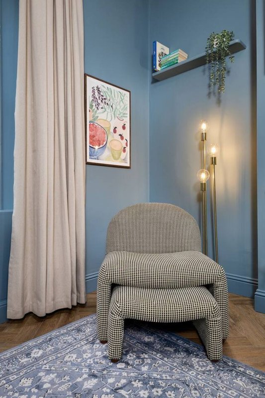 Modern bedroom corner with upholstered chair, blue wall, framed artwork and floating shelf