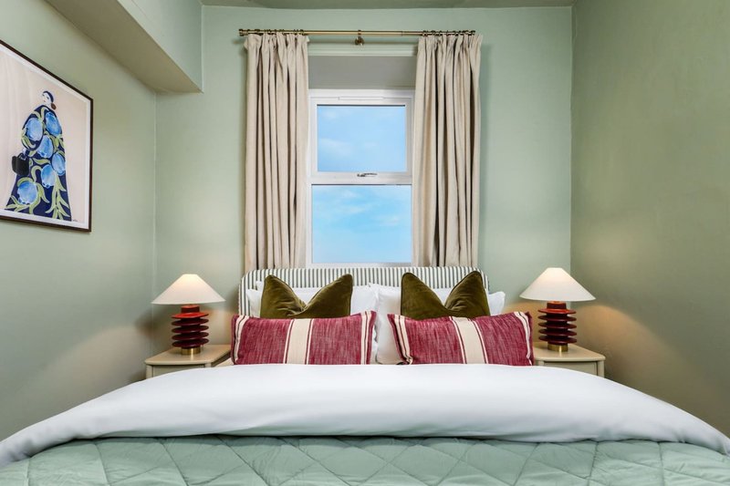 Bright bedroom with double bed, red and white striped bedding, olive cushions, bedside lamps and window with sea view