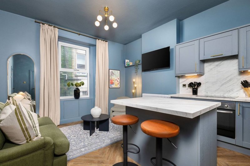 Open-plan kitchen and living area with blue walls, island seating, and green sofa