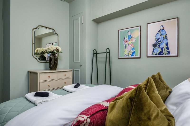 Modern bedroom with double beds, wooden dresser, mirror, wall art and gold cushions