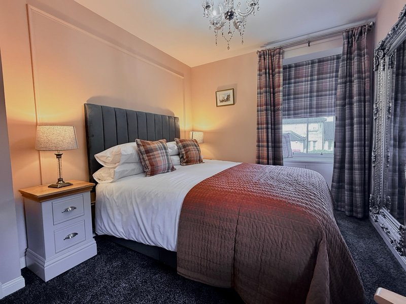Bedroom with double bed, dark headboard, white bedside table, warm lighting and patterned curtains