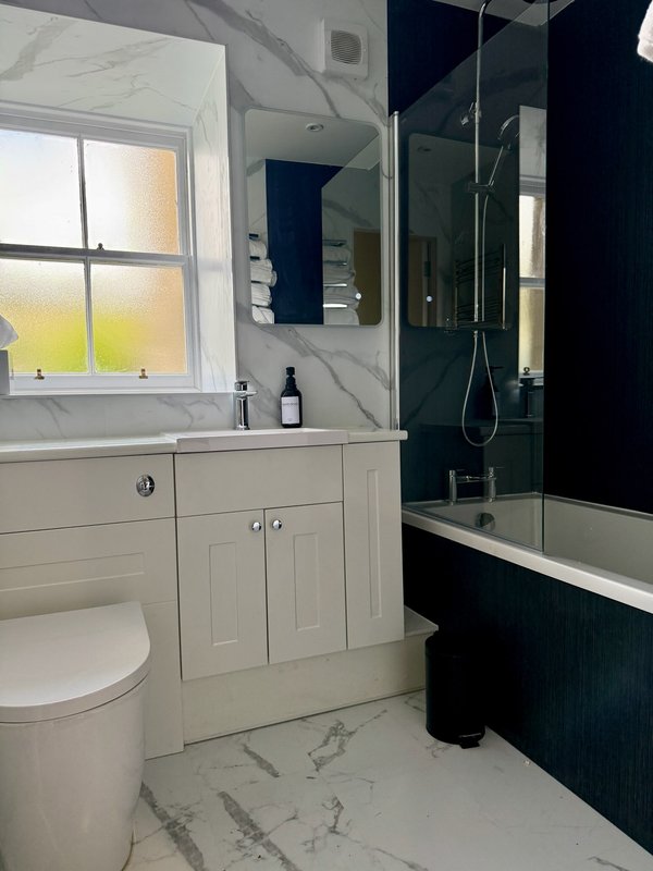 Modern bathroom with white vanity, marble countertop, toilet, mirror and black shower enclosure