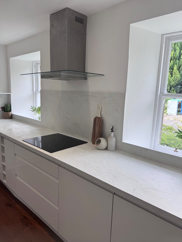Modern kitchen with white cabinetry, marble countertop, induction hob and grey extractor hood