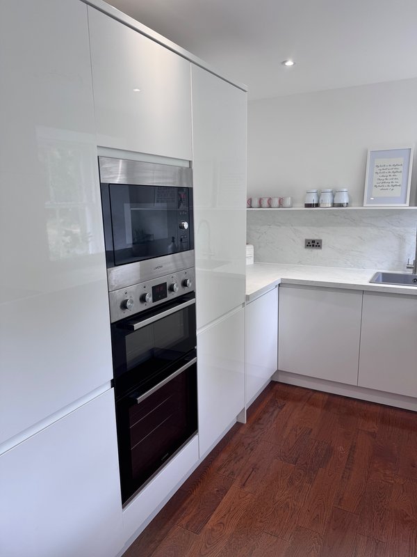 Modern white kitchen with built-in double oven, microwave, wooden flooring and open shelving