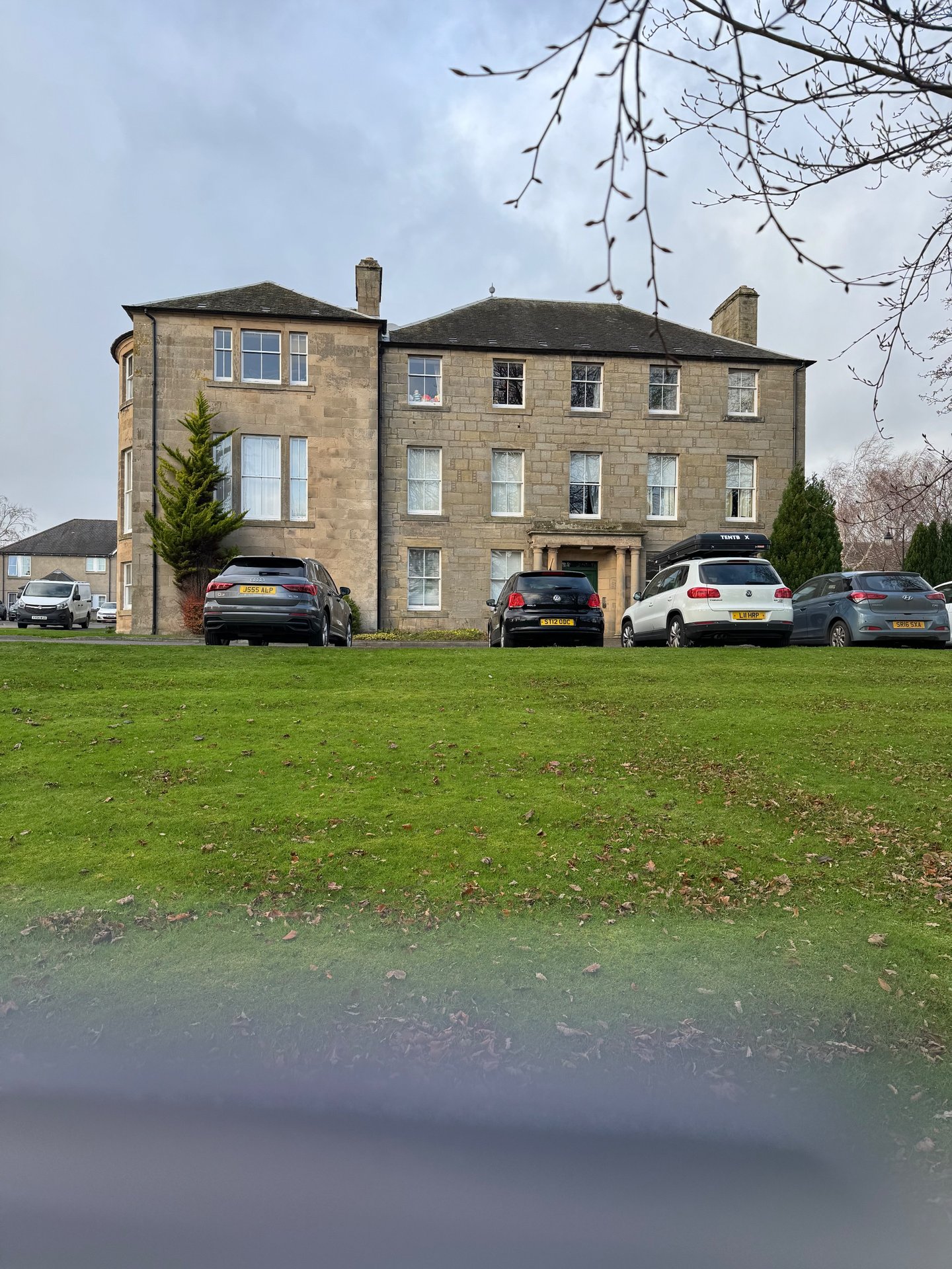 Stone period property with multiple windows, parked cars on grass forecourt
