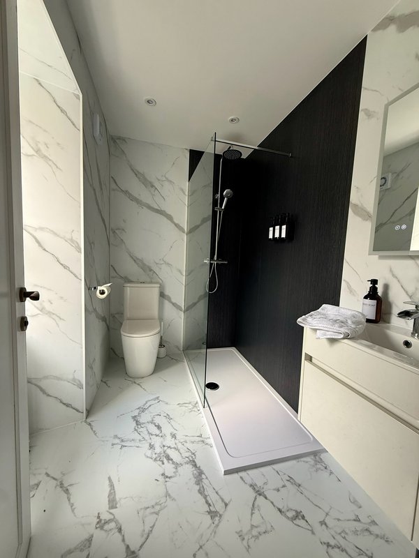 Modern bathroom with marble tiles, walk-in shower, toilet, and white vanity unit